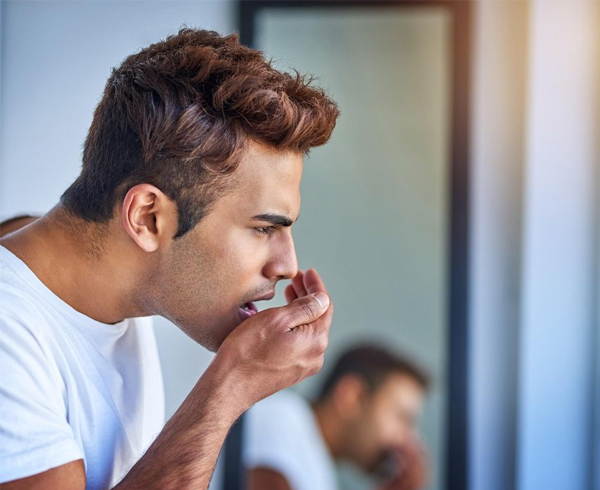 Man in white shirt touching mouth thoughtfully in dental office setting with blurred background.