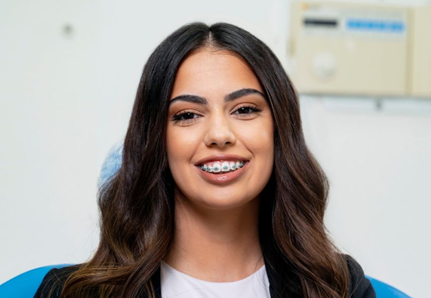 Smiling woman with long dark hair in dental office setting wearing blue scrubs.