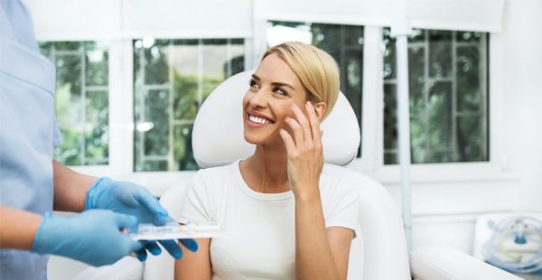 Woman on phone in dental office wearing white, smiling during consultation with dentist.