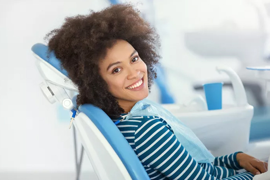 Smiling woman relaxing in blue dental chair at modern dental office.