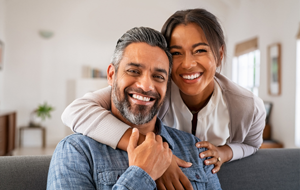 Happy couple hugging on couch in bright home interior, smiling at camera