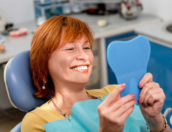 Woman holding blue heart shape smiling in dental office chair.