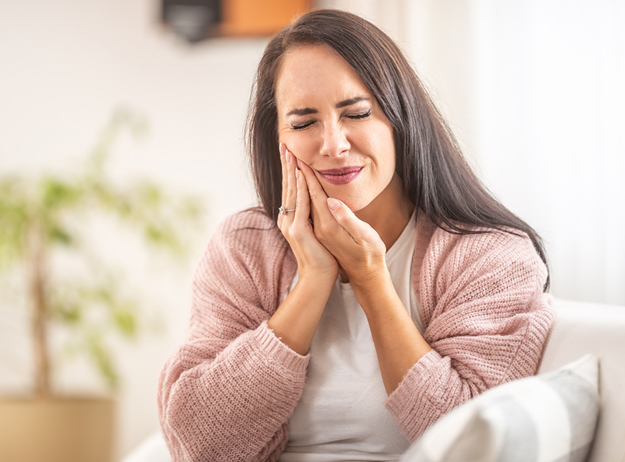 Woman smiling with hands to face in bright dental office setting with plants