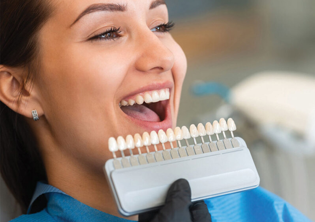 Woman smiling while holding dental shade guide for tooth color matching at dental office.