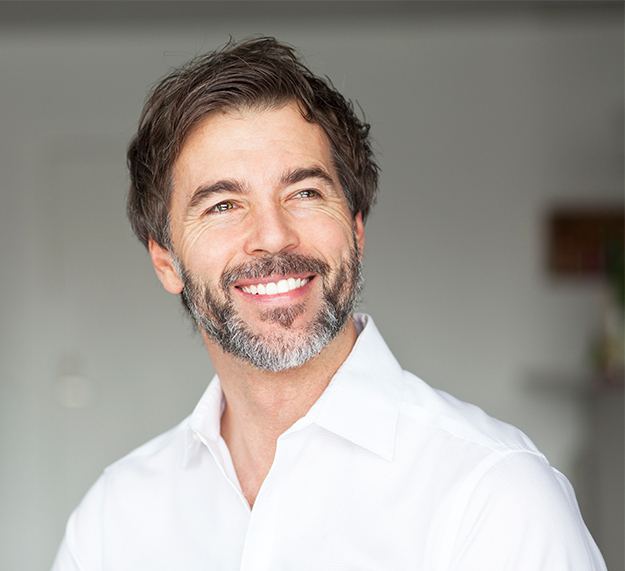 Professional headshot of smiling man in white shirt against neutral dental office background.