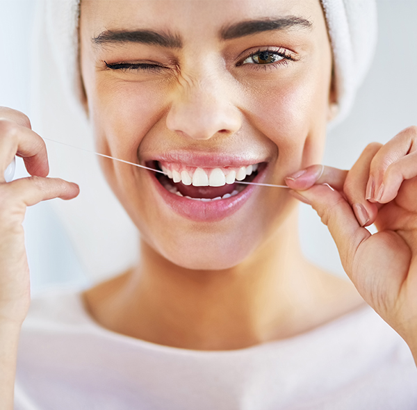 Happy woman flossing teeth, demonstrating dental hygiene in bright, clean setting.