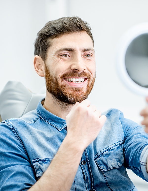 Man smiling at dental mirror in modern dental office setting