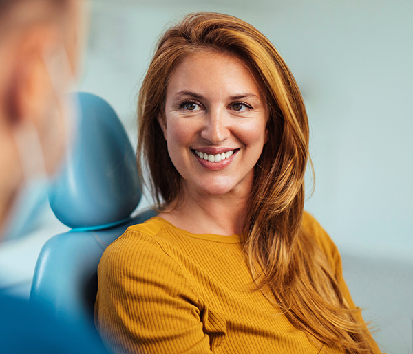 Smiling woman in yellow shirt seated in blue dental chair at Aspire Dental office.