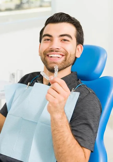Smiling male patient in dental chair holding blue bib at Aspire Dental office.