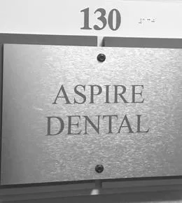 Aspire Dental office sign with room number 130 mounted on wall with two fasteners.