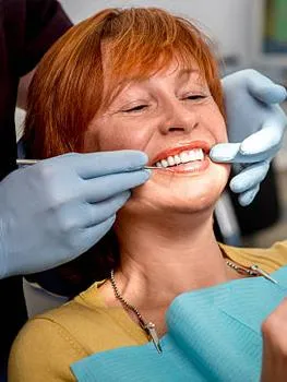 Woman receiving dental examination from dentist wearing gloves in clinical setting.