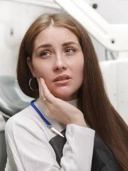 Woman in dental office uniform touching face thoughtfully, professional healthcare setting.