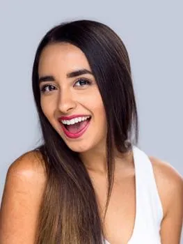 Woman smiling at camera wearing white tank top against neutral background.